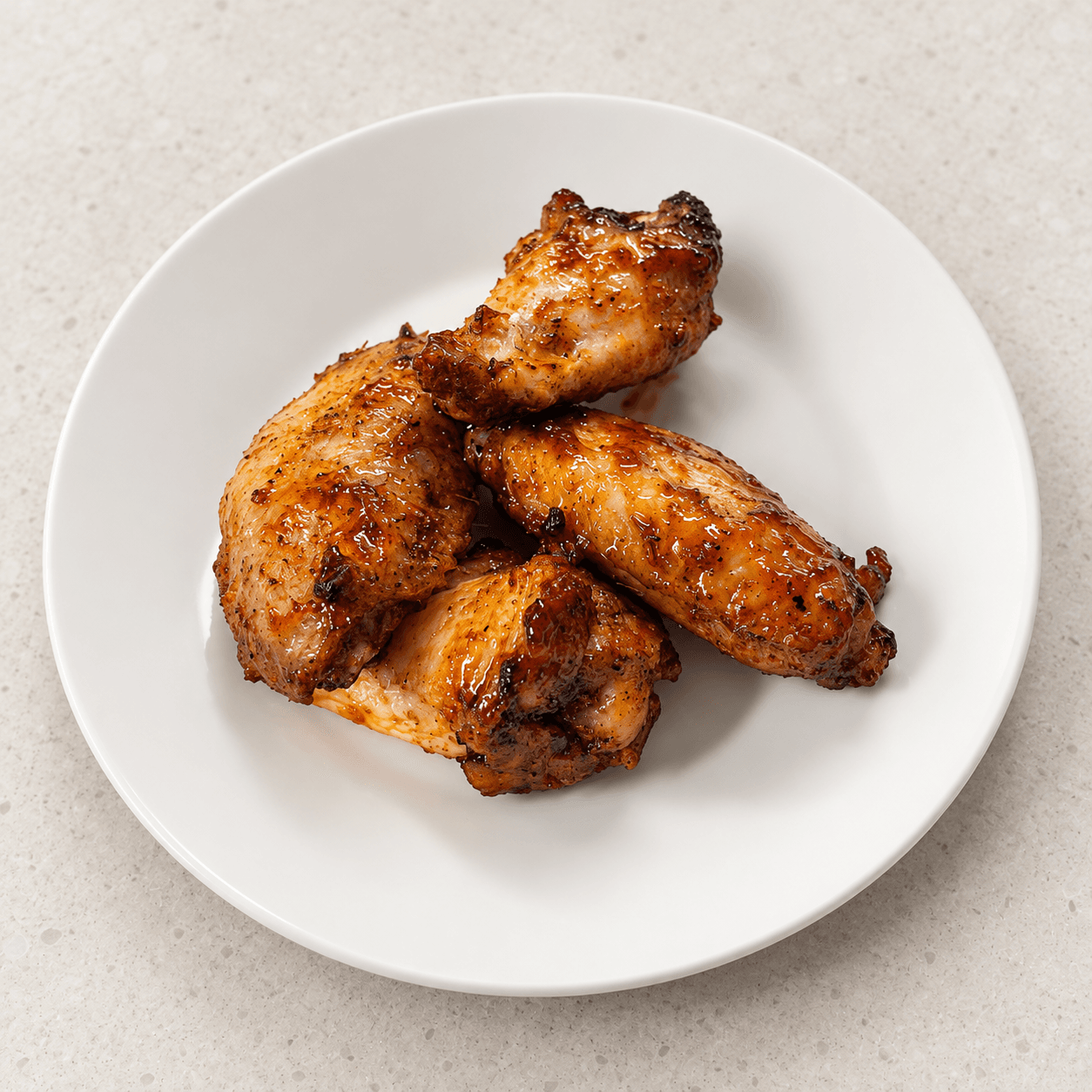 Four roasted chicken wings with a golden-brown glaze served on a plain white plate.